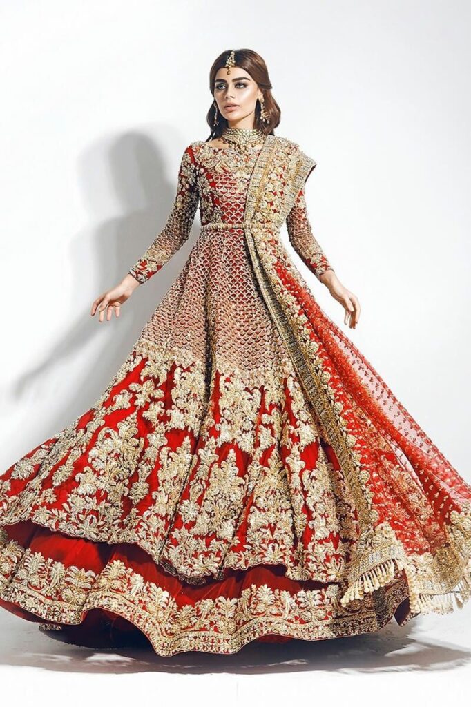 Bride twirling in a red and gold embroidered bridal gown with a layered flared skirt and a draped dupatta Bride twirling in a red and gold embroidered bridal gown with a layered flared skirt and a draped dupatta